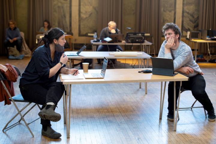 two people speaking across a desk during rehearsals